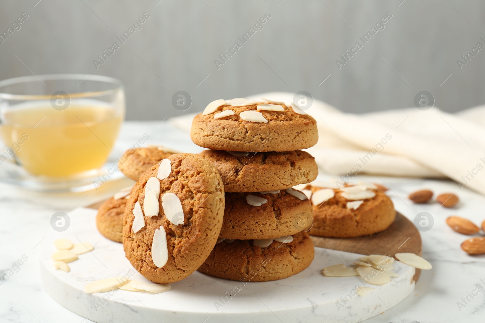 Photo of Tasty cookies with almond flakes and tea on white marble table, closeup