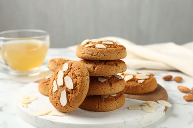 Photo of Tasty cookies with almond flakes and tea on white marble table, closeup