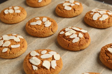 Photo of Tasty cookies with almond flakes on parchment paper, closeup