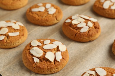 Photo of Tasty cookies with almond flakes on parchment paper, closeup