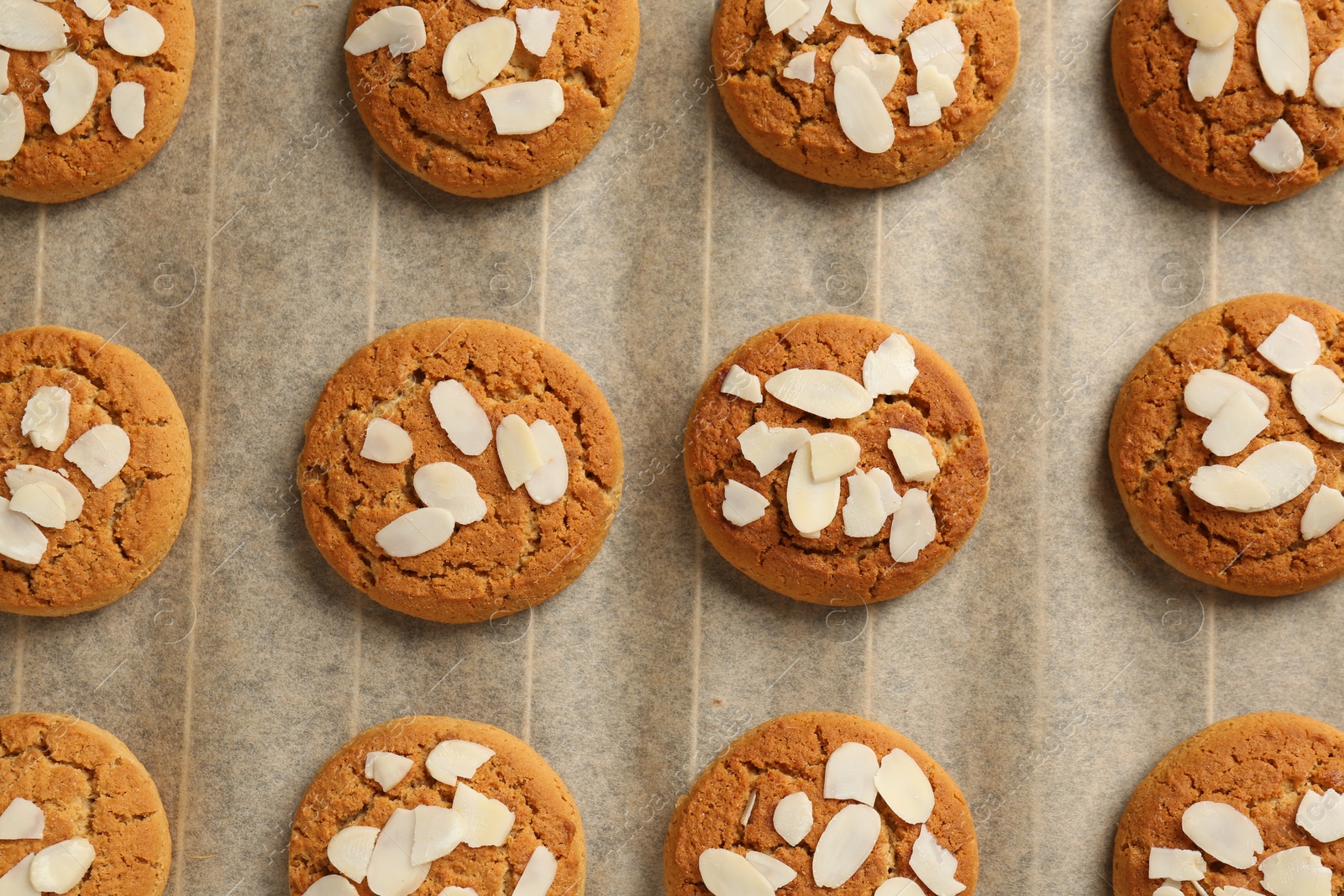 Photo of Tasty cookies with almond flakes on parchment paper, top view