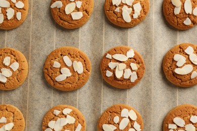 Photo of Tasty cookies with almond flakes on parchment paper, top view