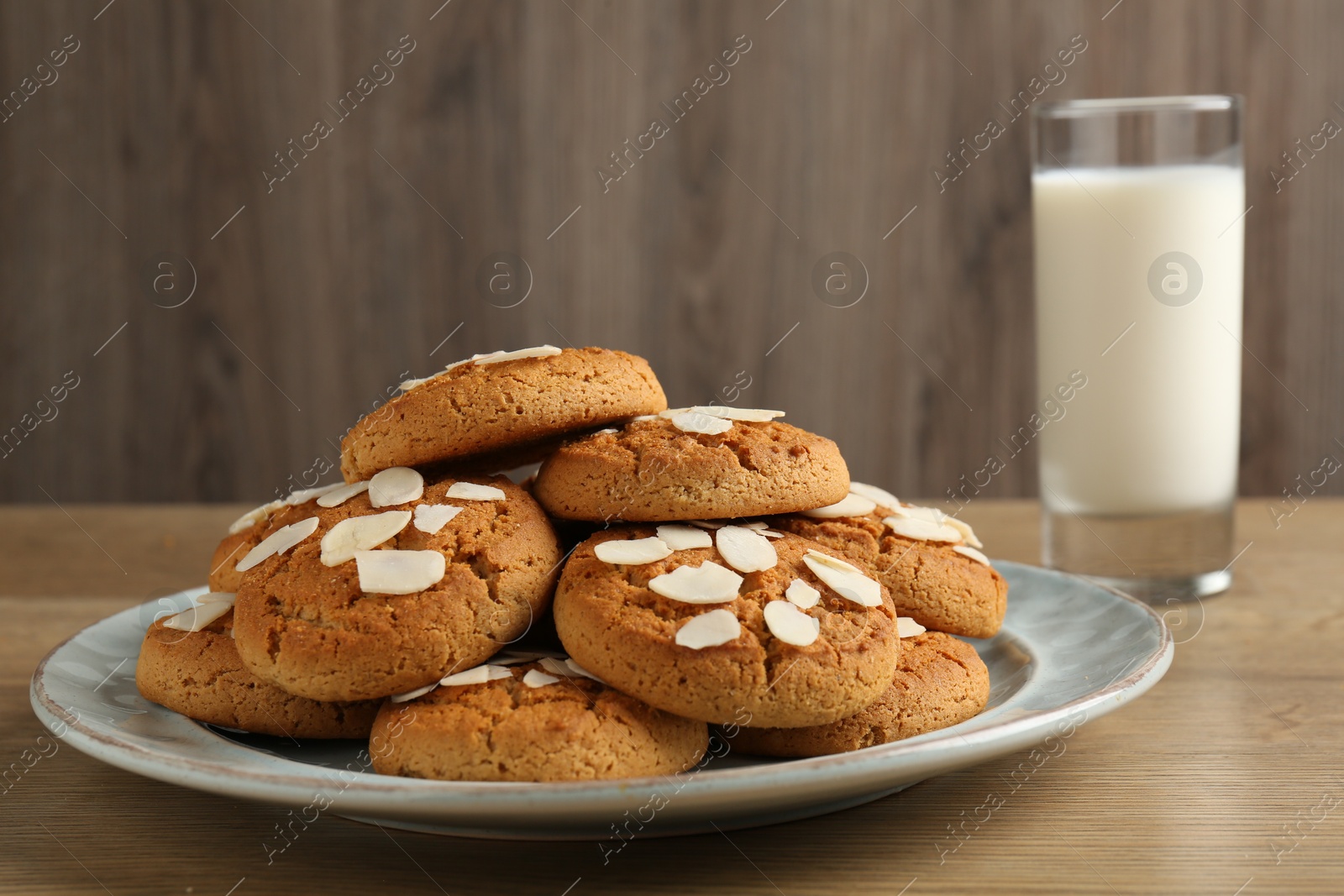 Photo of Tasty cookies with almond flakes and milk on wooden table, closeup