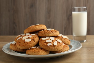 Photo of Tasty cookies with almond flakes and milk on wooden table, closeup