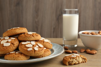 Photo of Tasty cookies with almond flakes, nuts and milk on wooden table, closeup