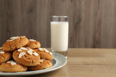 Photo of Tasty cookies with almond flakes and milk on wooden table, closeup. Space for text