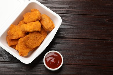 Photo of Tasty chicken nuggets and sauce on wooden table, top view. Space for text