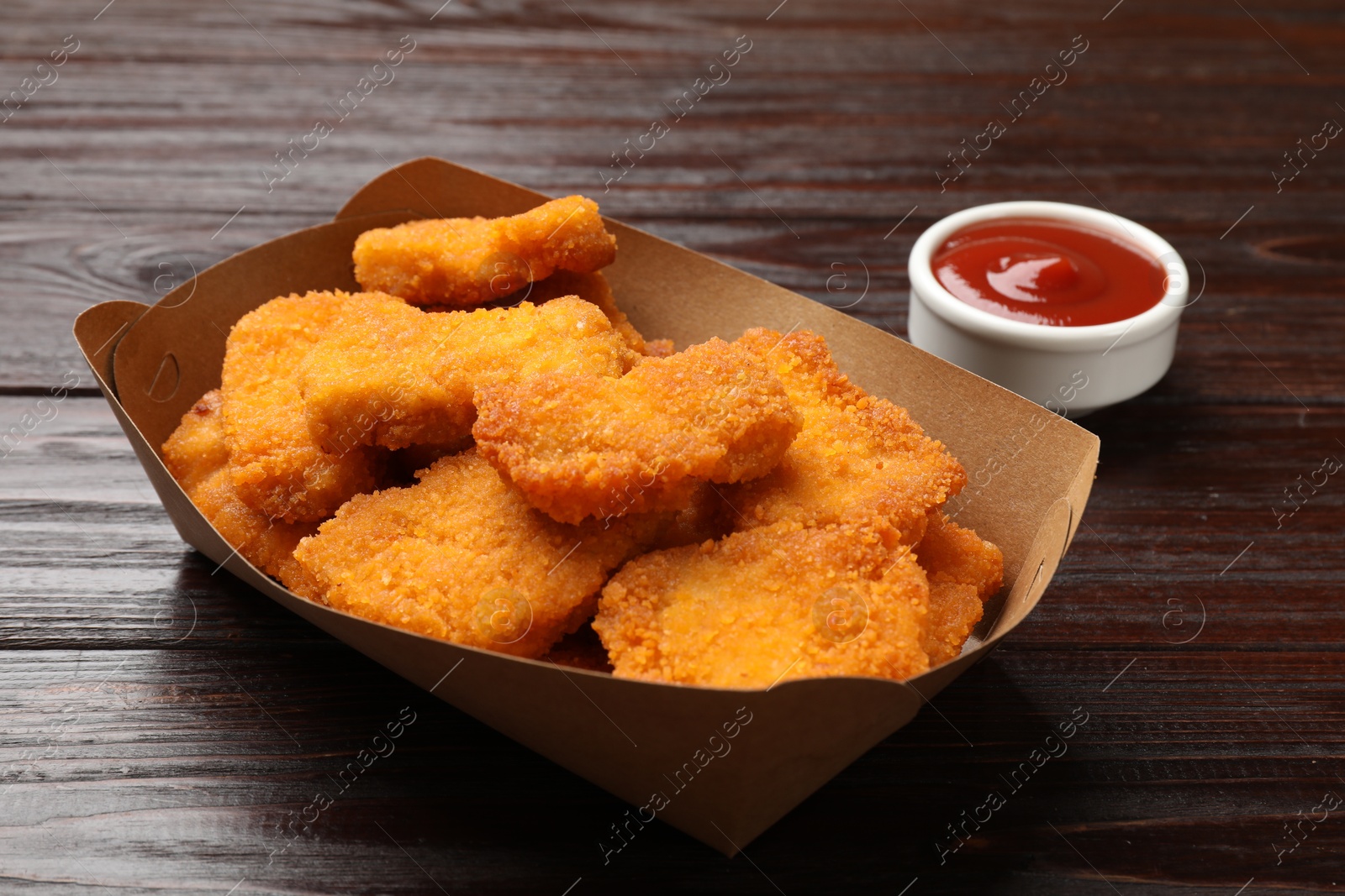 Photo of Tasty chicken nuggets in paper container and sauce on wooden table, closeup