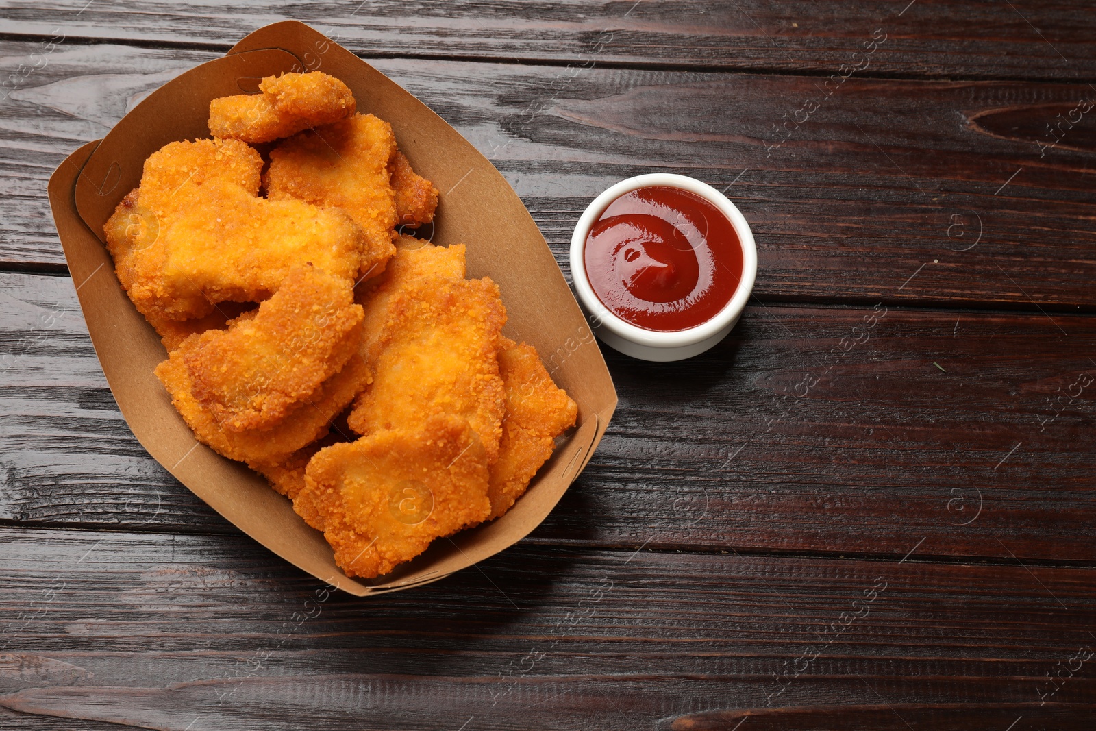 Photo of Tasty chicken nuggets in paper container and sauce on wooden table, top view. Space for text