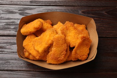 Photo of Tasty chicken nuggets in paper container on wooden table, top view