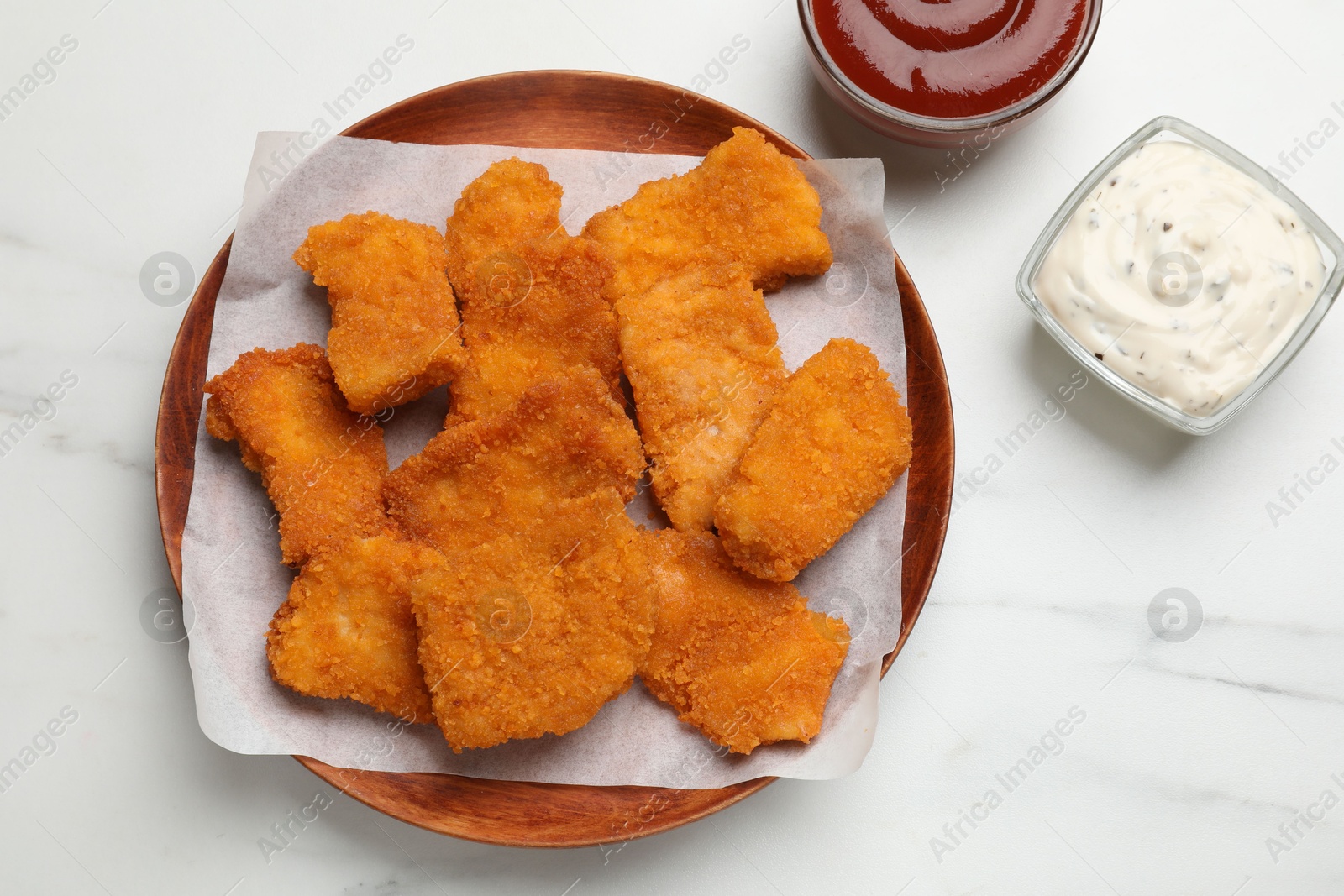 Photo of Tasty chicken nuggets and sauces on white marble table, top view