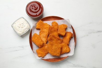 Photo of Tasty chicken nuggets and sauces on white marble table, top view