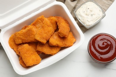 Photo of Tasty chicken nuggets and sauces on white marble table, top view