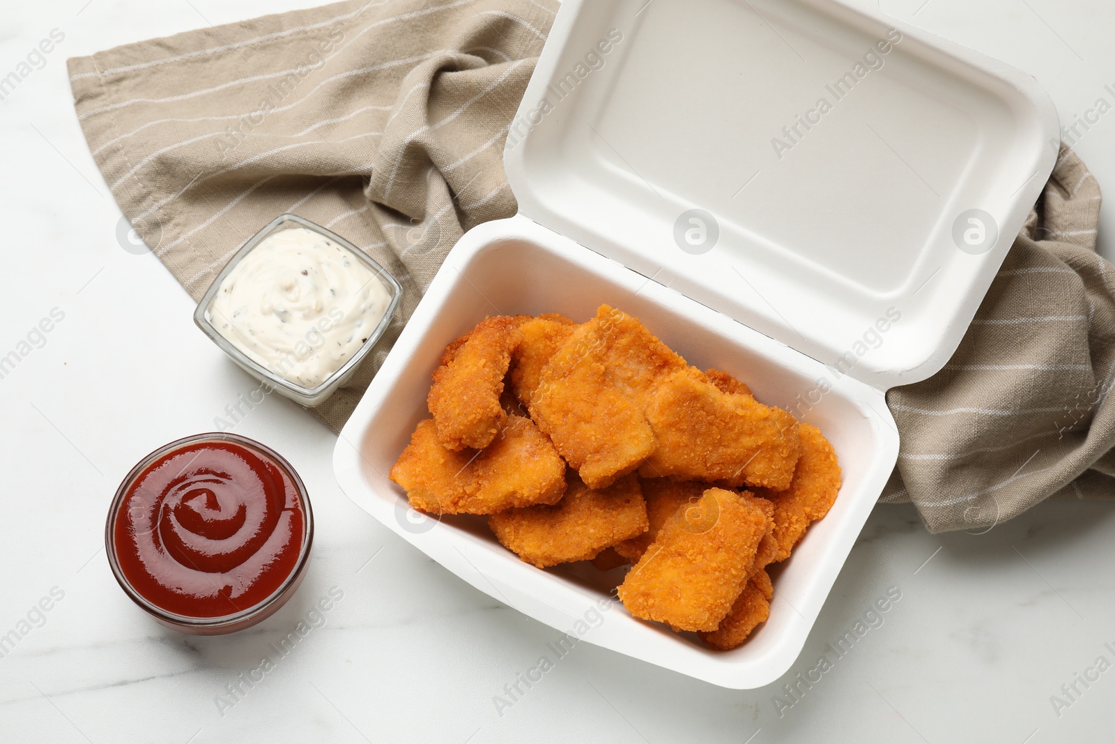 Photo of Tasty chicken nuggets and sauces on white marble table, top view