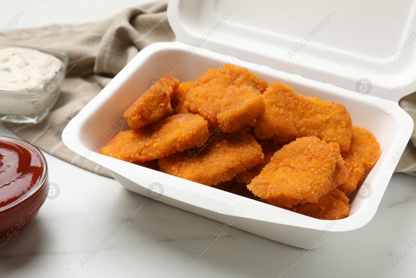 Photo of Tasty chicken nuggets and sauces on white marble table, closeup