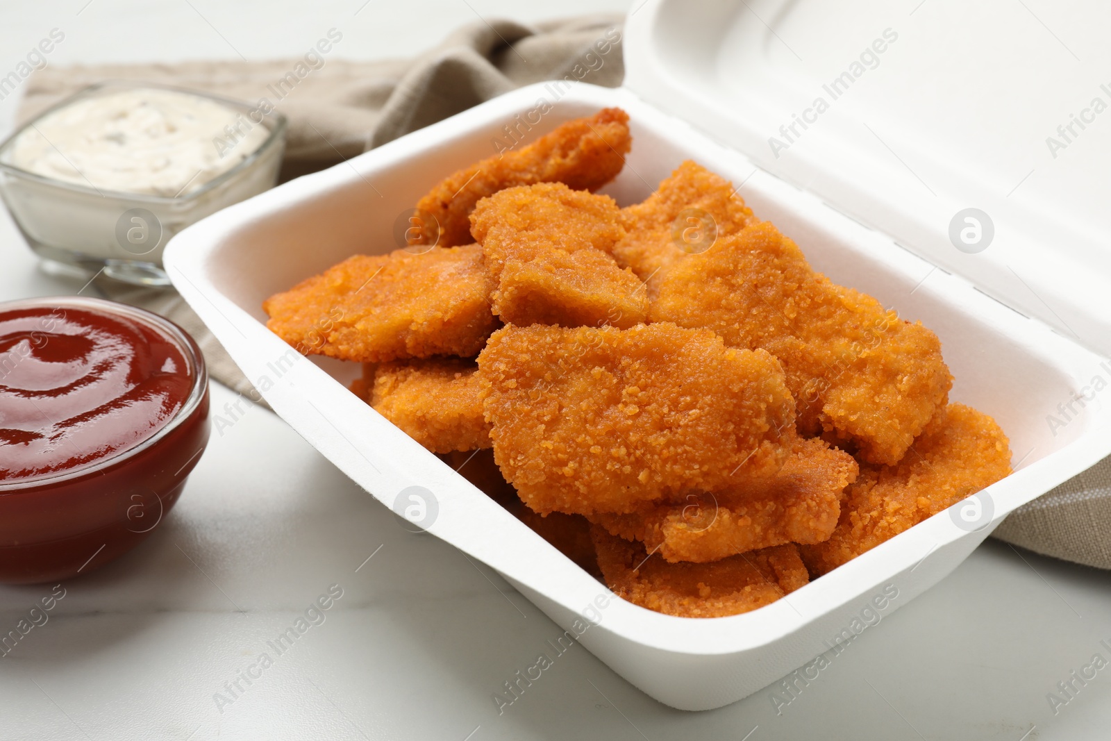 Photo of Tasty chicken nuggets and sauces on white marble table, closeup