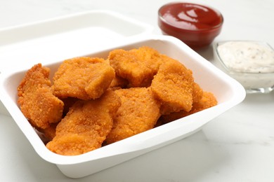 Photo of Tasty chicken nuggets and sauces on white marble table, closeup