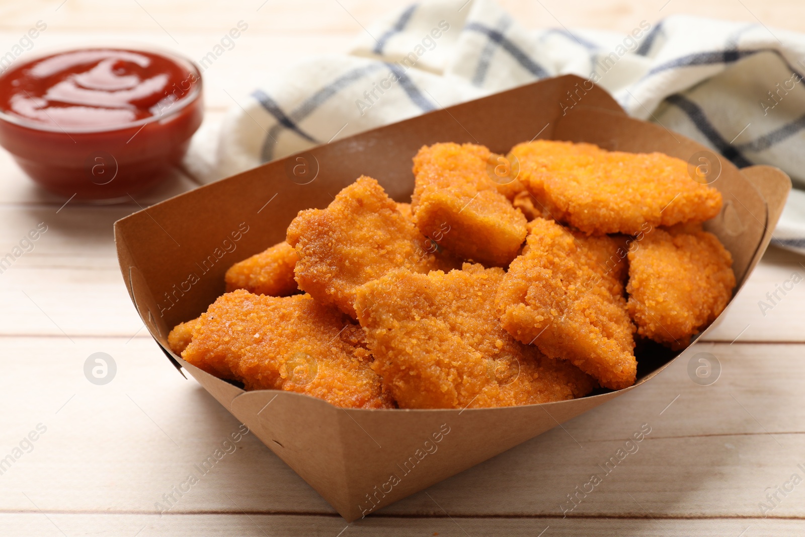 Photo of Tasty chicken nuggets in paper container and sauce on wooden table, closeup