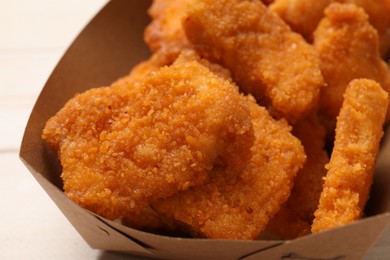 Photo of Tasty chicken nuggets in paper container on table, closeup