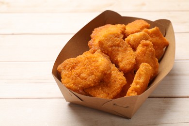 Photo of Tasty chicken nuggets in paper container on wooden table, closeup