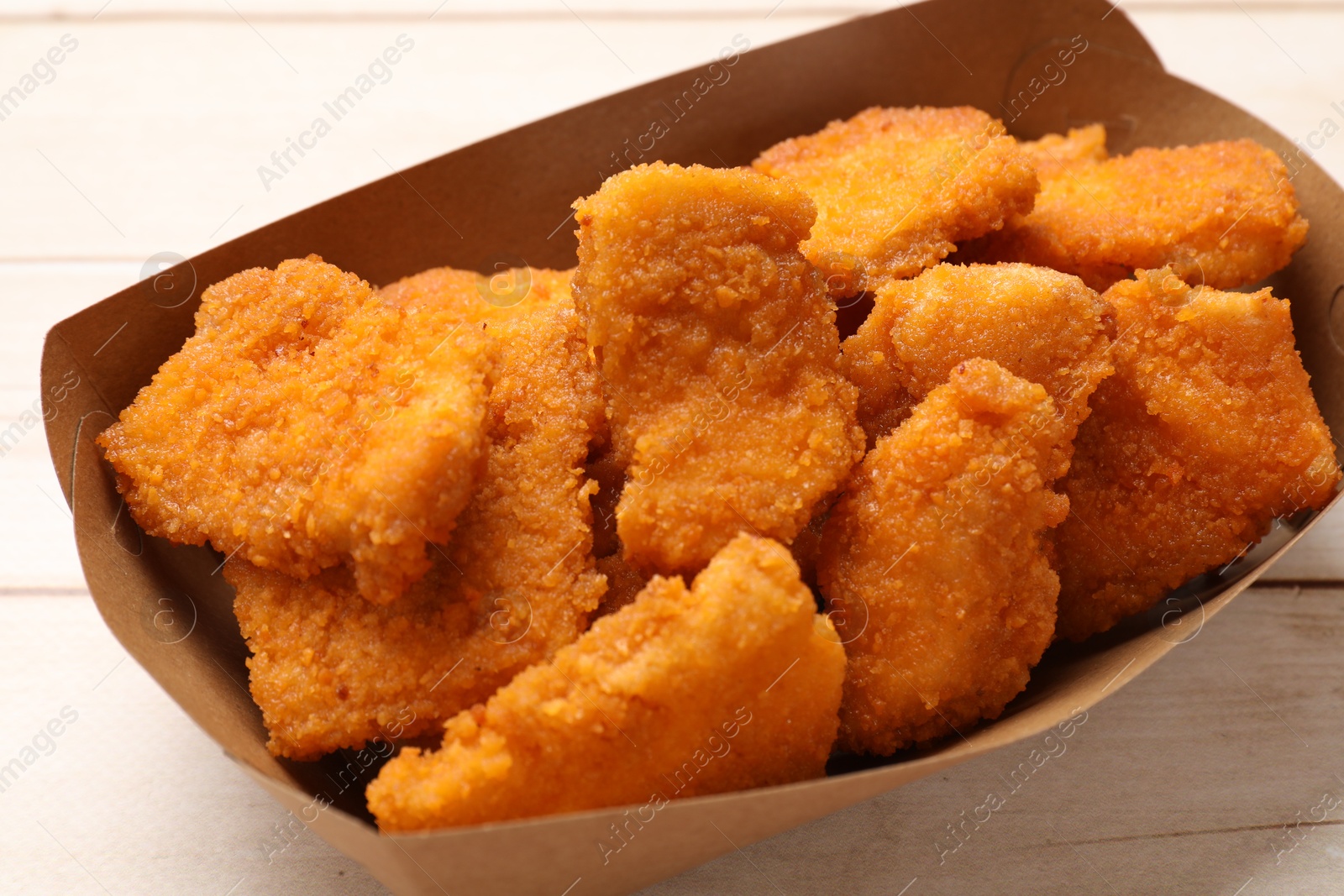 Photo of Tasty chicken nuggets in paper container on wooden table, closeup