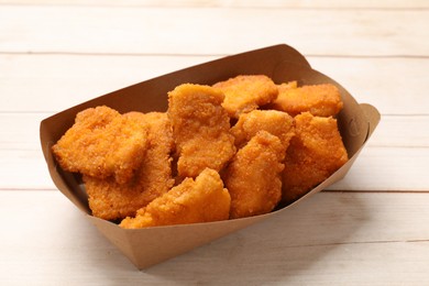 Photo of Tasty chicken nuggets in paper container on wooden table, closeup