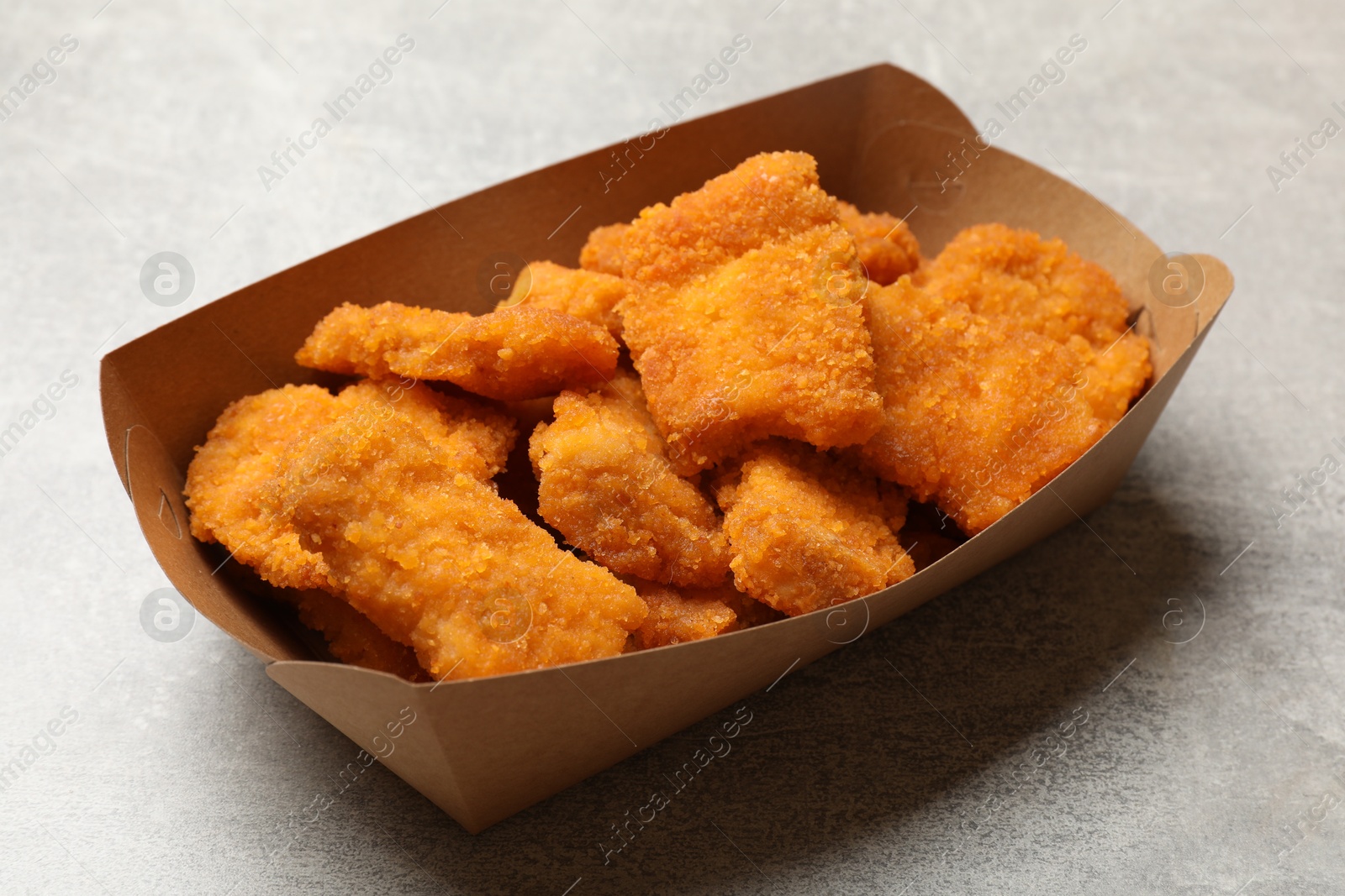 Photo of Delicious chicken nuggets in carton box on light table, closeup