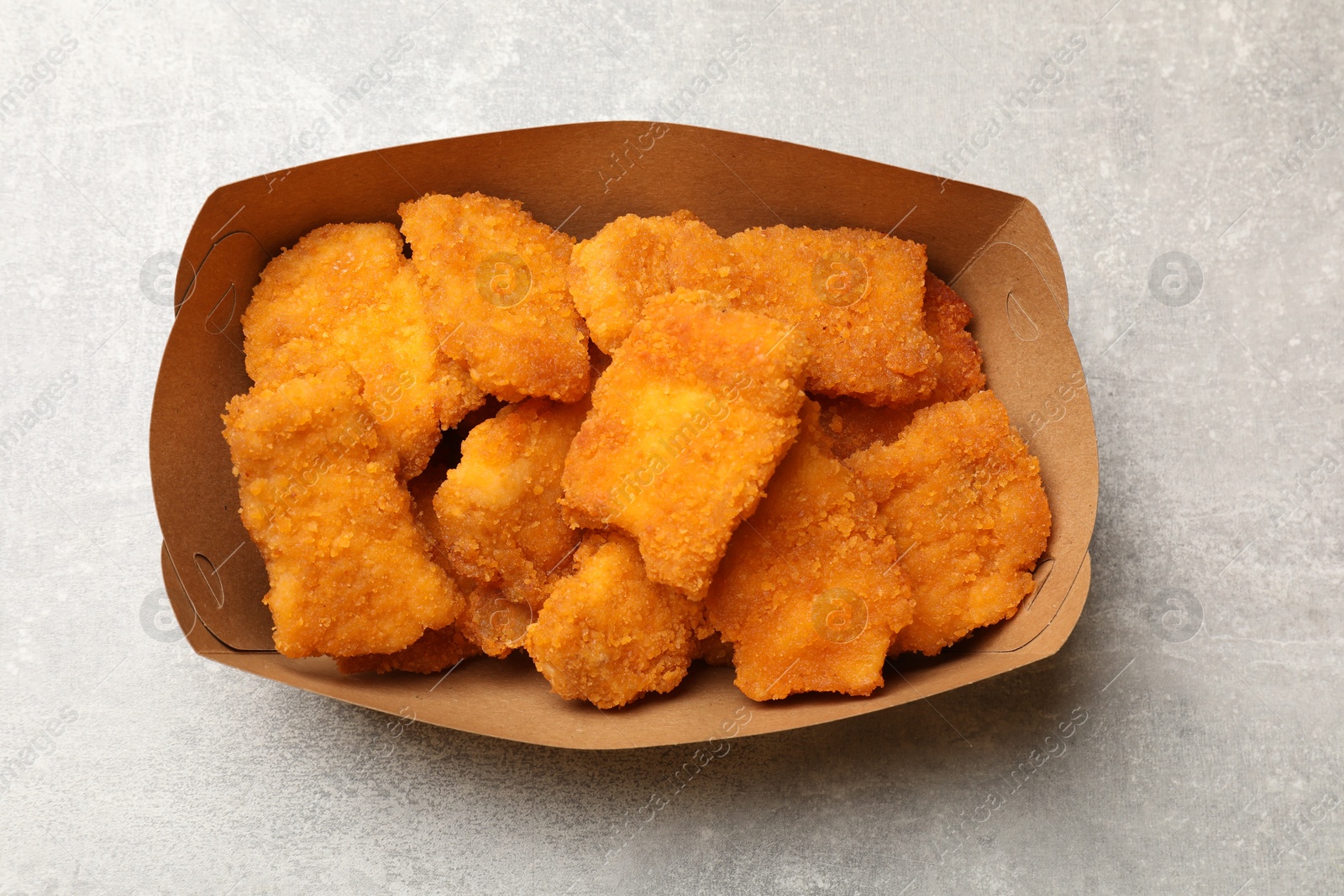 Photo of Delicious chicken nuggets in carton box on light table, top view