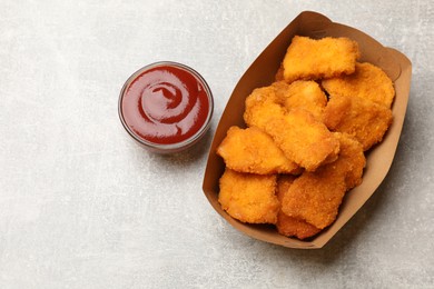 Photo of Delicious chicken nuggets in carton box and ketchup on light table, top view