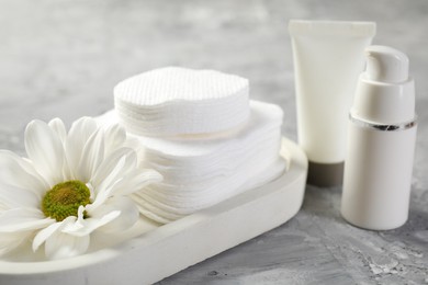 Photo of Clean cotton pads, cosmetic products and flower on grey table, closeup