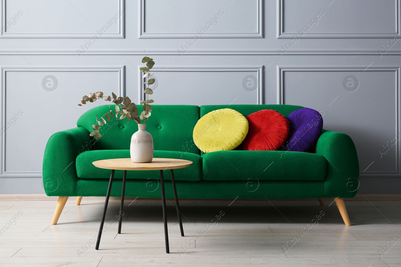 Image of Stylish green sofa with cushions and table in room