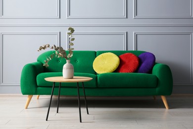 Image of Stylish green sofa with cushions and table in room