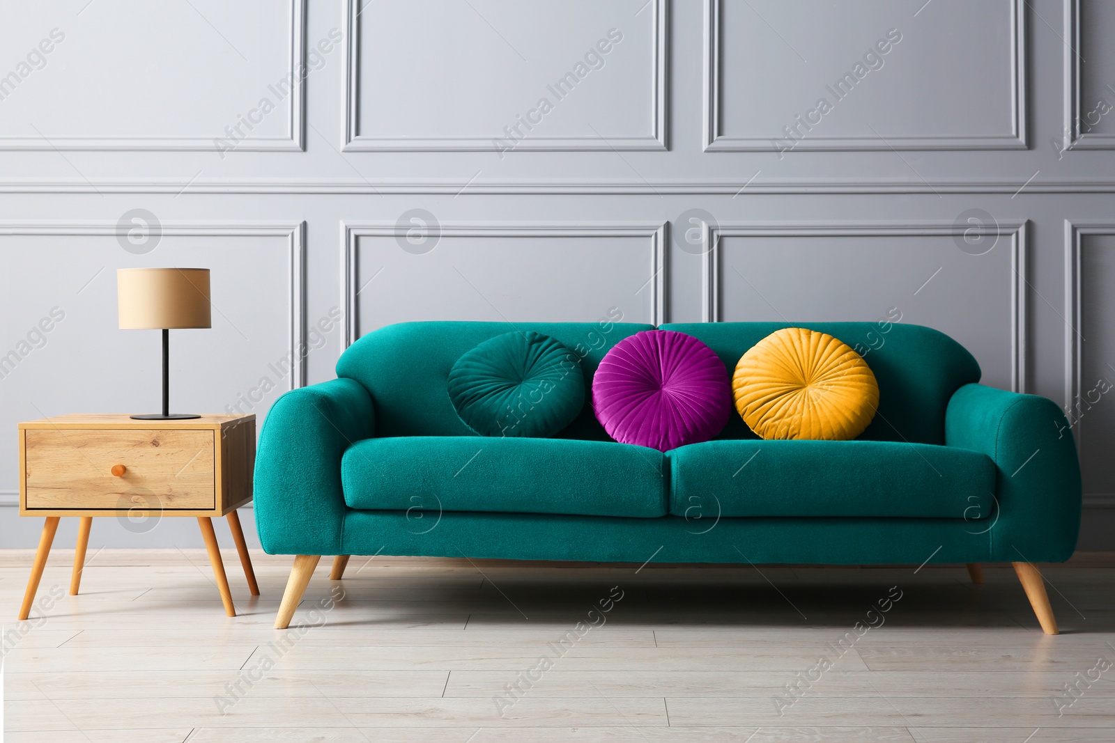 Image of Stylish teal color sofa with cushions and table near grey wall