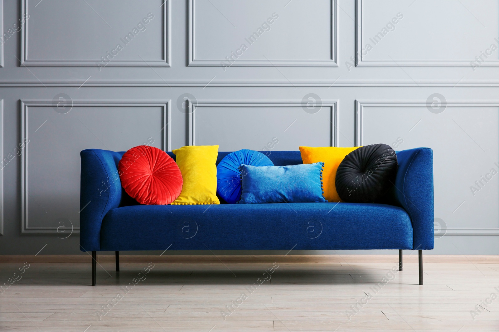 Image of Stylish blue sofa with cushions near grey wall