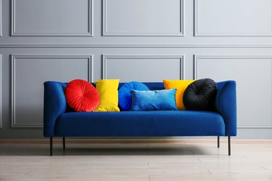 Image of Stylish blue sofa with cushions near grey wall