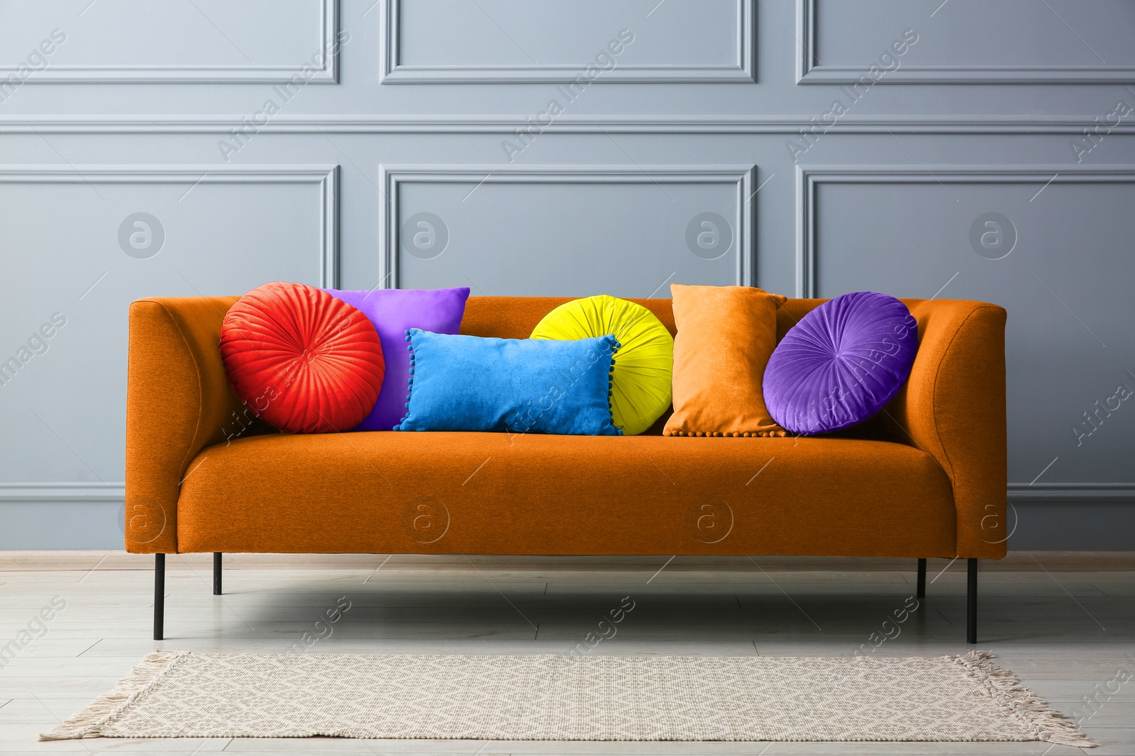 Image of Stylish orange sofa with cushions near grey wall