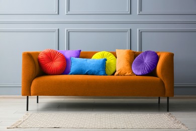 Image of Stylish orange sofa with cushions near grey wall