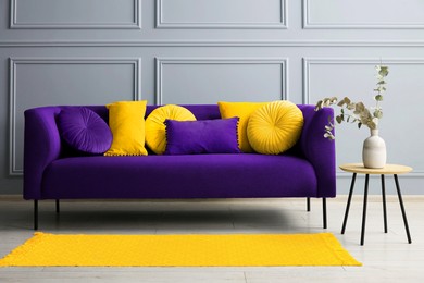 Image of Stylish sofa with cushions and table near grey wall