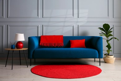 Image of Comfortable dark blue sofa, houseplant and table near grey wall in room