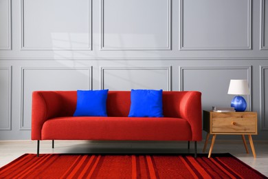 Image of Comfortable red sofa and side table near grey wall in room