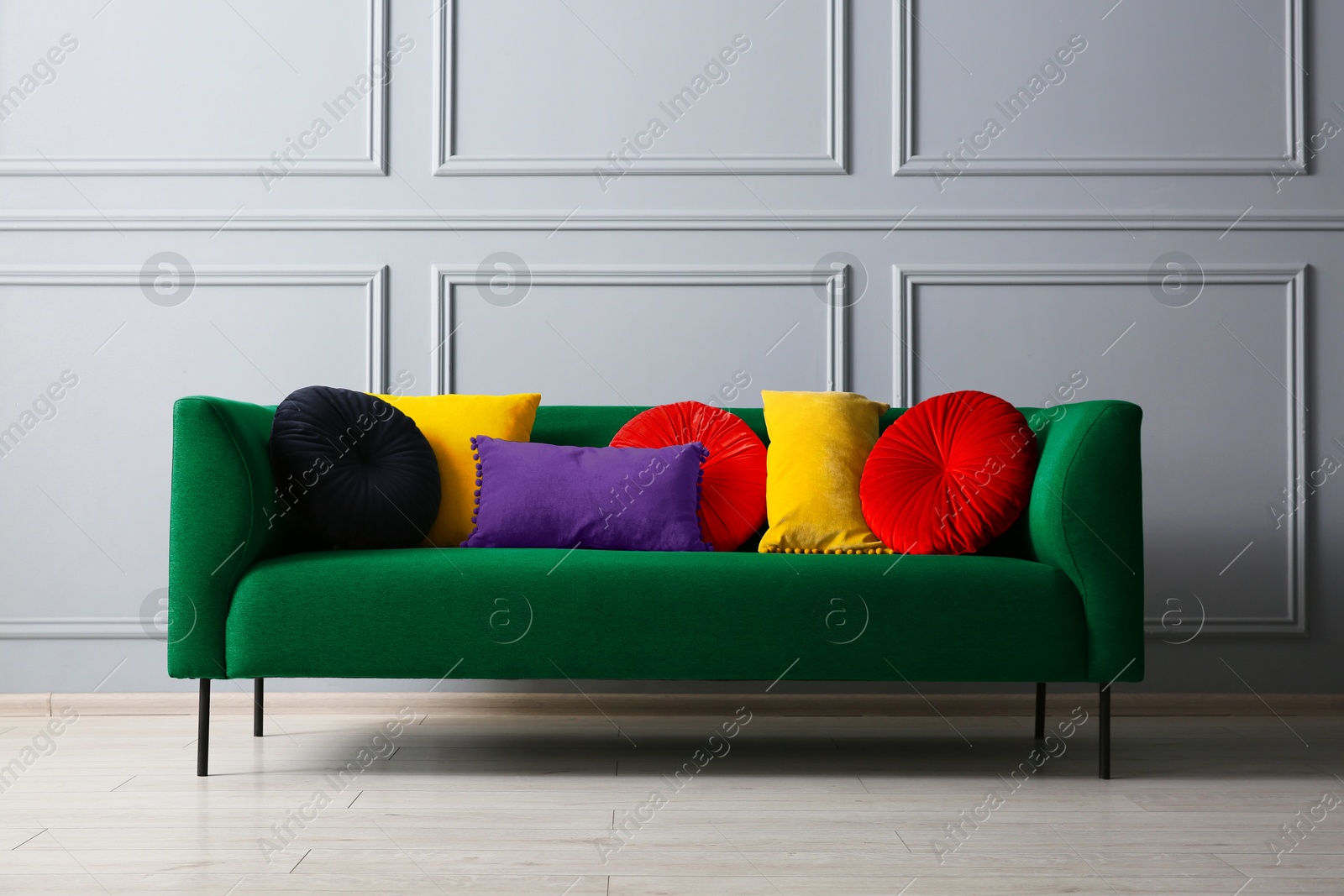 Image of Stylish green sofa with different cushions near grey wall