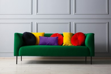 Image of Stylish green sofa with different cushions near grey wall