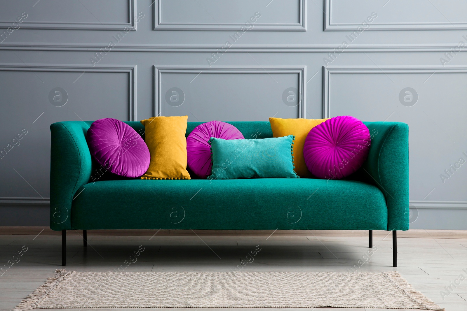 Image of Stylish teal color sofa with different cushions near grey wall