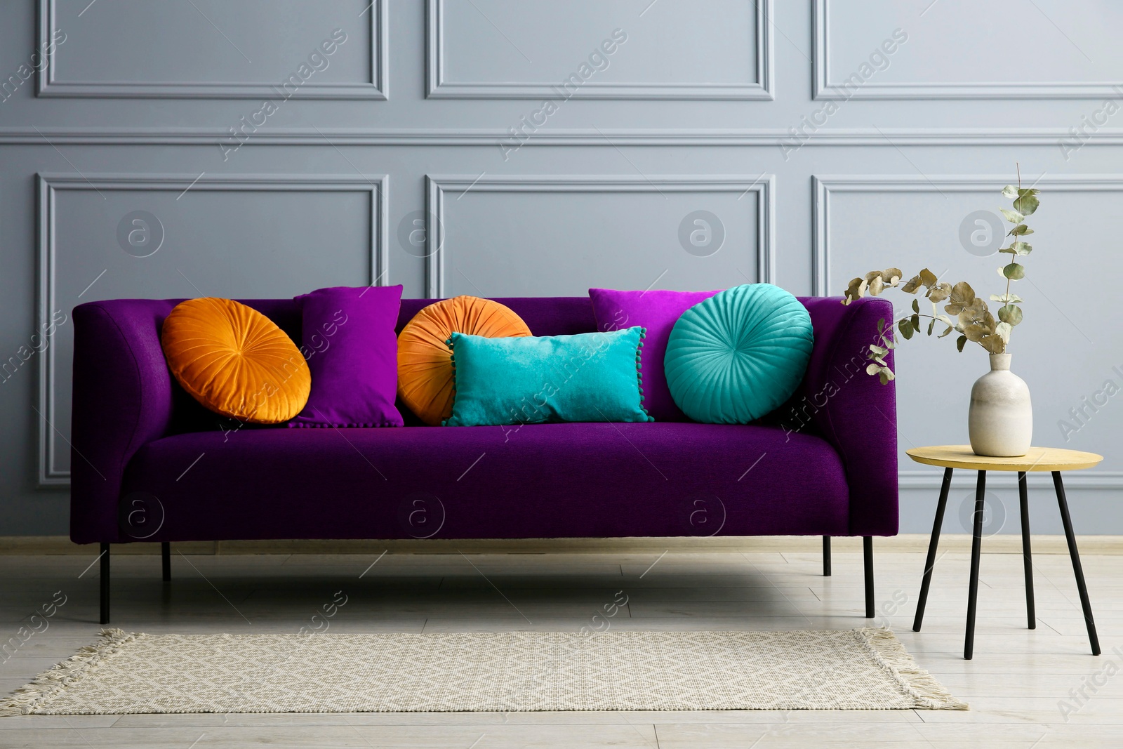 Image of Stylish purple sofa with cushions and table near grey wall