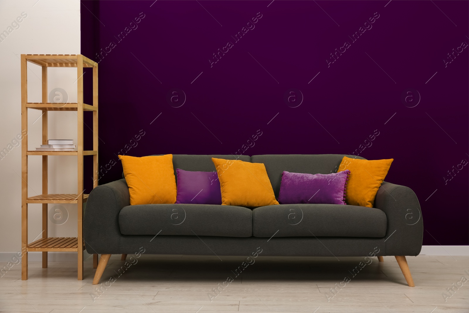 Image of Stylish grey sofa with pillows and shelving unit near purple wall indoors