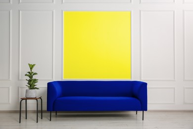 Image of Stylish blue sofa and side table near wall with yellow accent