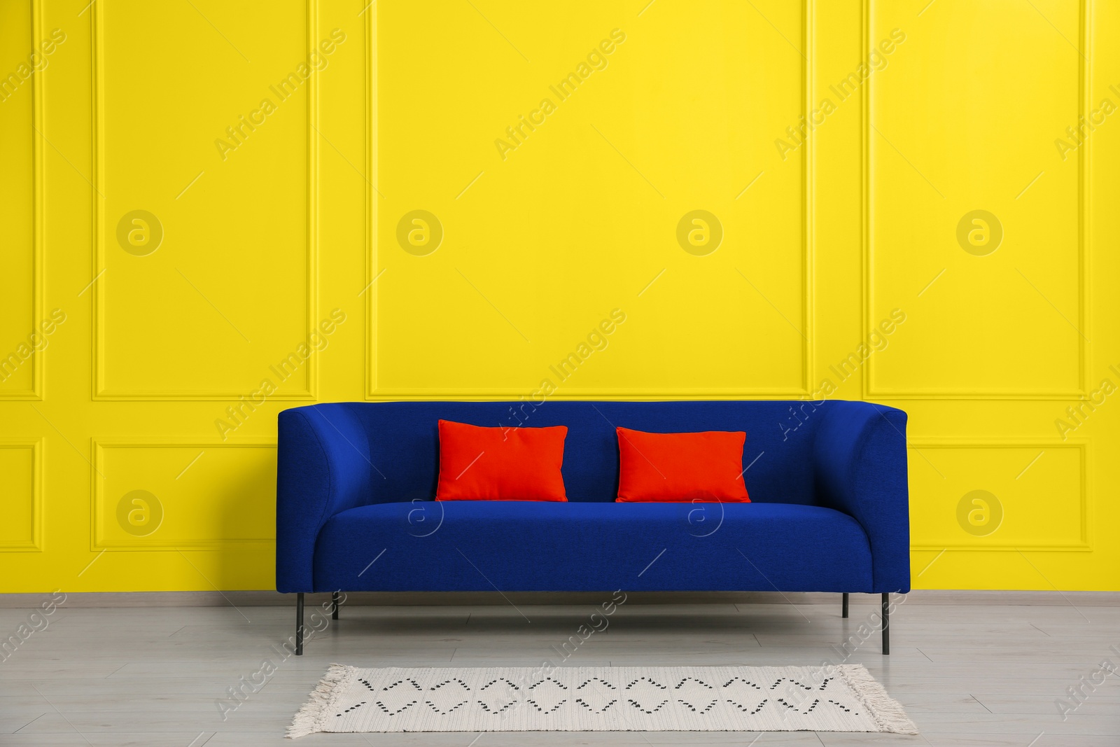 Image of Stylish blue sofa with red cushions near yellow wall