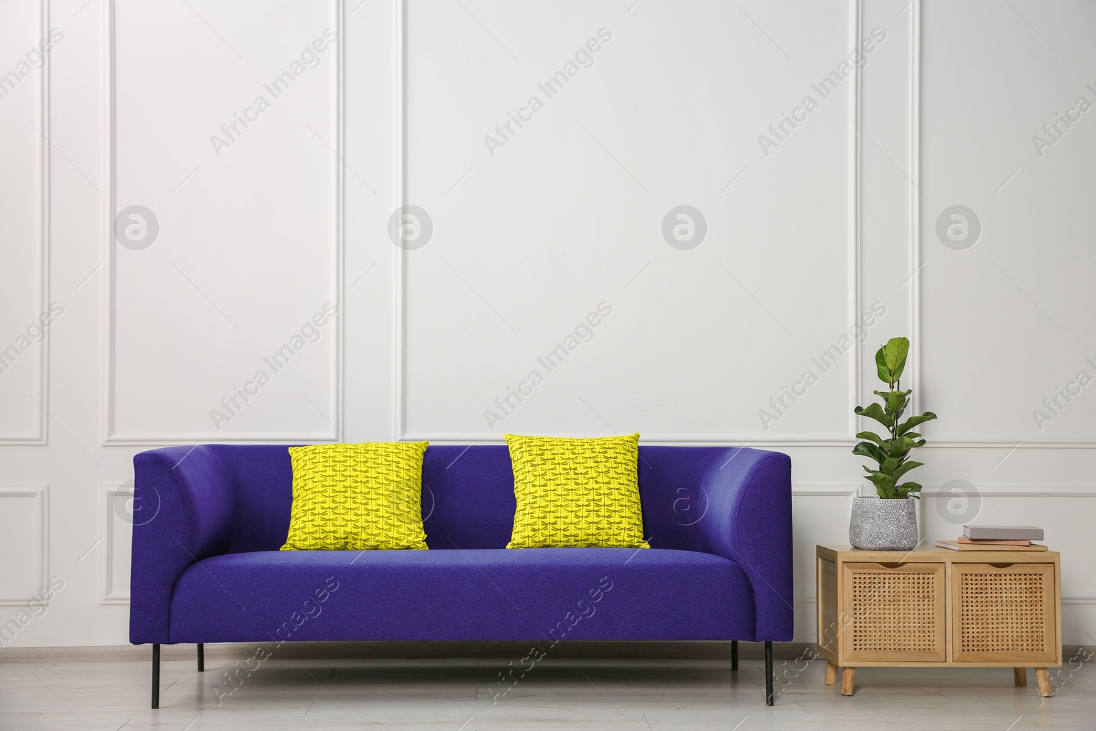 Image of Stylish sofa with cushions and on side table near white wall