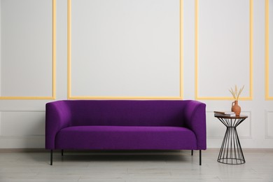 Image of Stylish purple sofa and side table near white wall with orange accent indoors