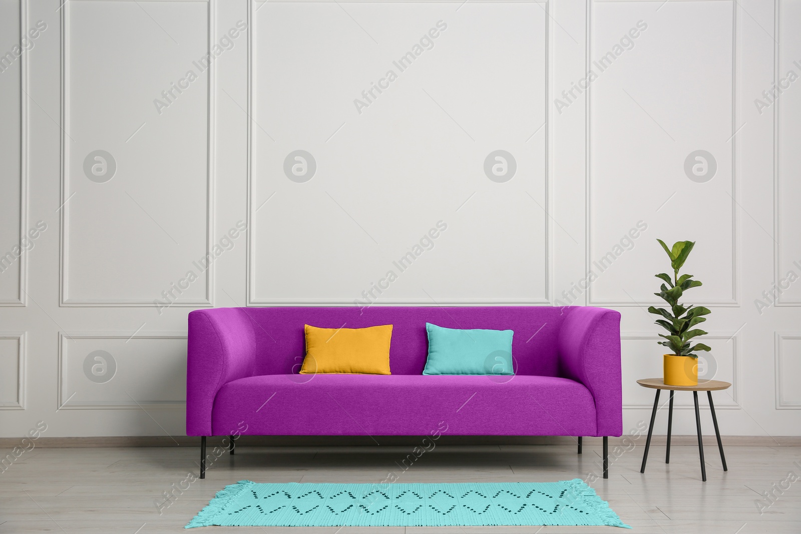 Image of Stylish magenta color sofa, pillows and table near white wall indoors